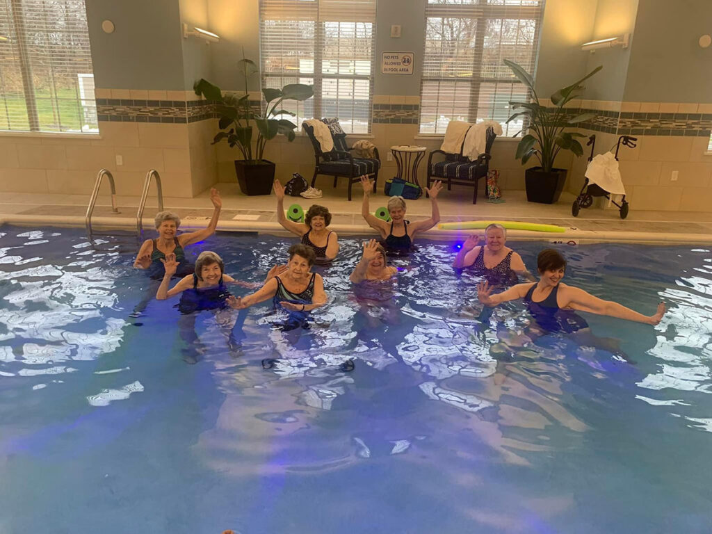 Aqua aerobics class with participants doing water exercises using foam dumbbells in a pool.