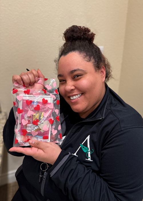 Senior living employee smiles while holding a festive Valentine’s-themed gift bag, celebrating Employee Appreciation Day with joy and gratitude.