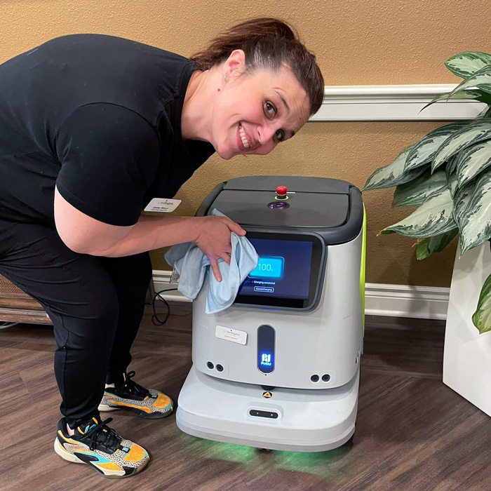 Smiling team member wiping down a service robot during spring cleaning at senior living community