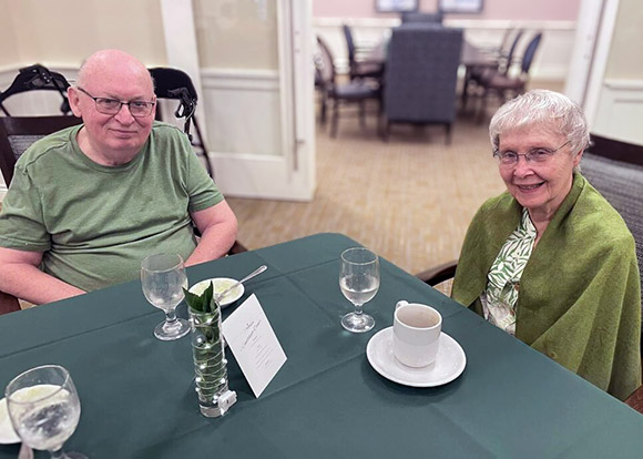A senior couple prepares to enjoy a chef-prepared meal at an elegantly set dining table.