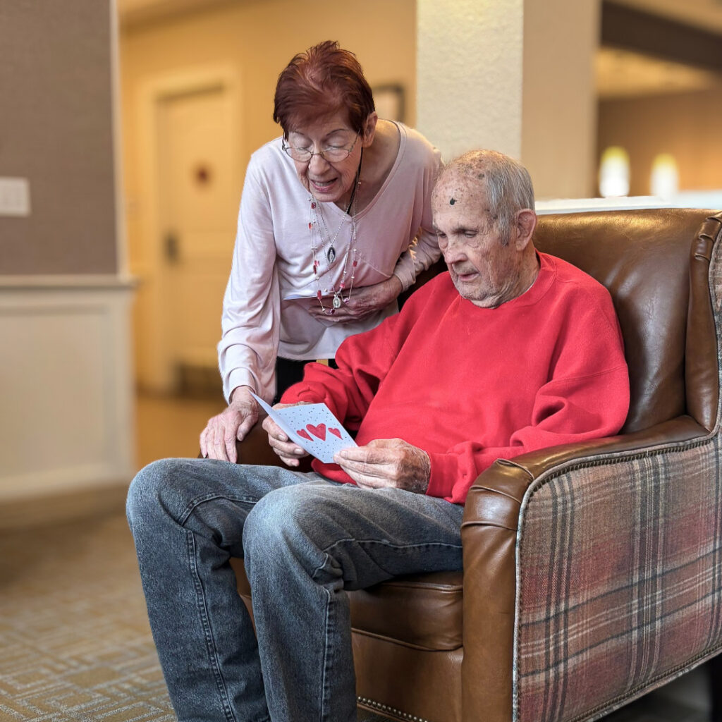 A senior man and loved one look at a greeting card with hearts on the cover at The Wellington Senior Living.